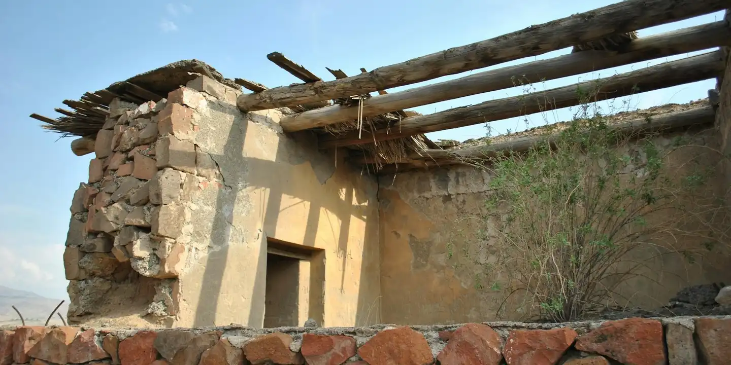A partially collapsed adobe roof with exposed wooden beams and crumbling walls