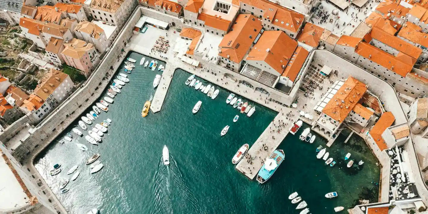 Aerial view of a coastal town with orange-tiled rooftops and a marina filled with boats.