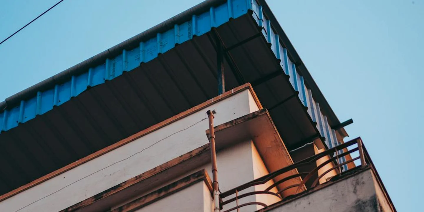 Side view of a metal roof with dark panels over a small residence, featuring an overhang and balcony, set against a clear blue sky.
