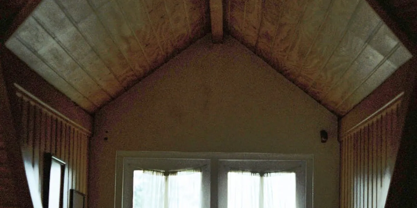 Attic interior with a pitched wooden roof and two small windows, softly lit from outside.