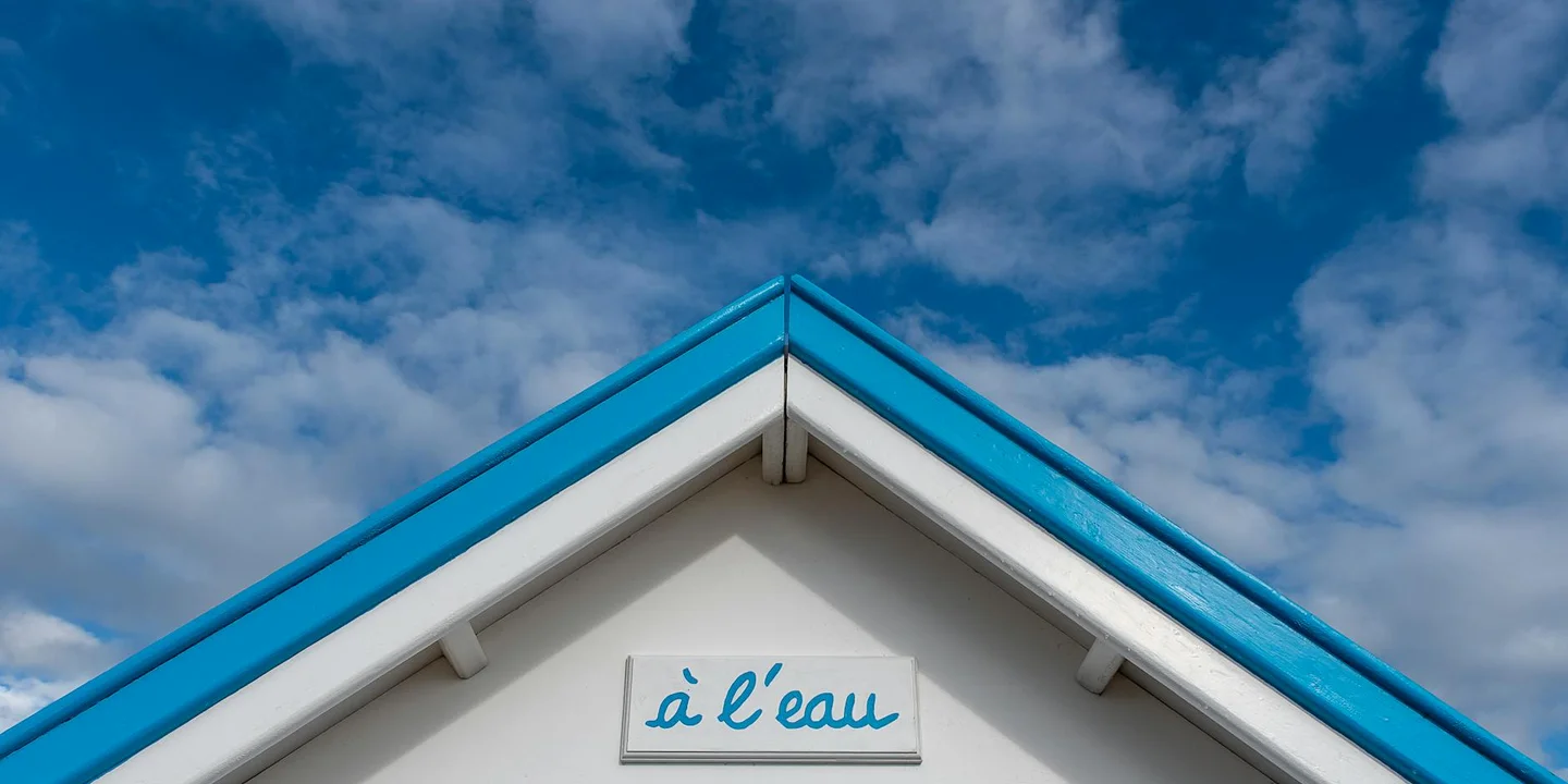 White building with a blue-trim shed roof under a partly cloudy sky; a sign on the facade reads 'L'eau'.