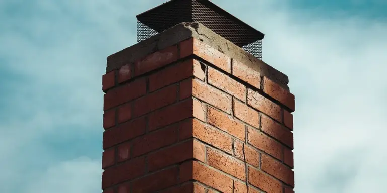 Brick chimney with a metal cap on top against a clear blue sky