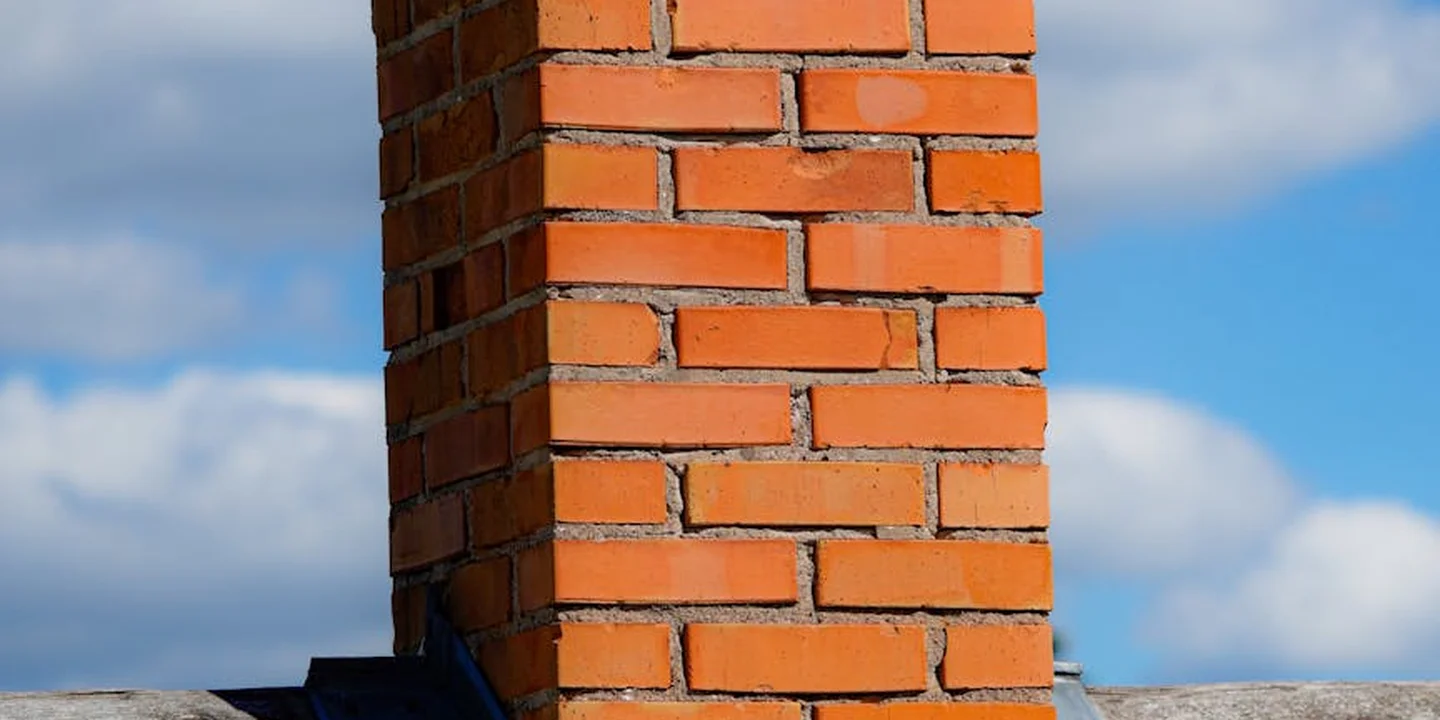 Brick chimney on a sloped roof against a blue sky