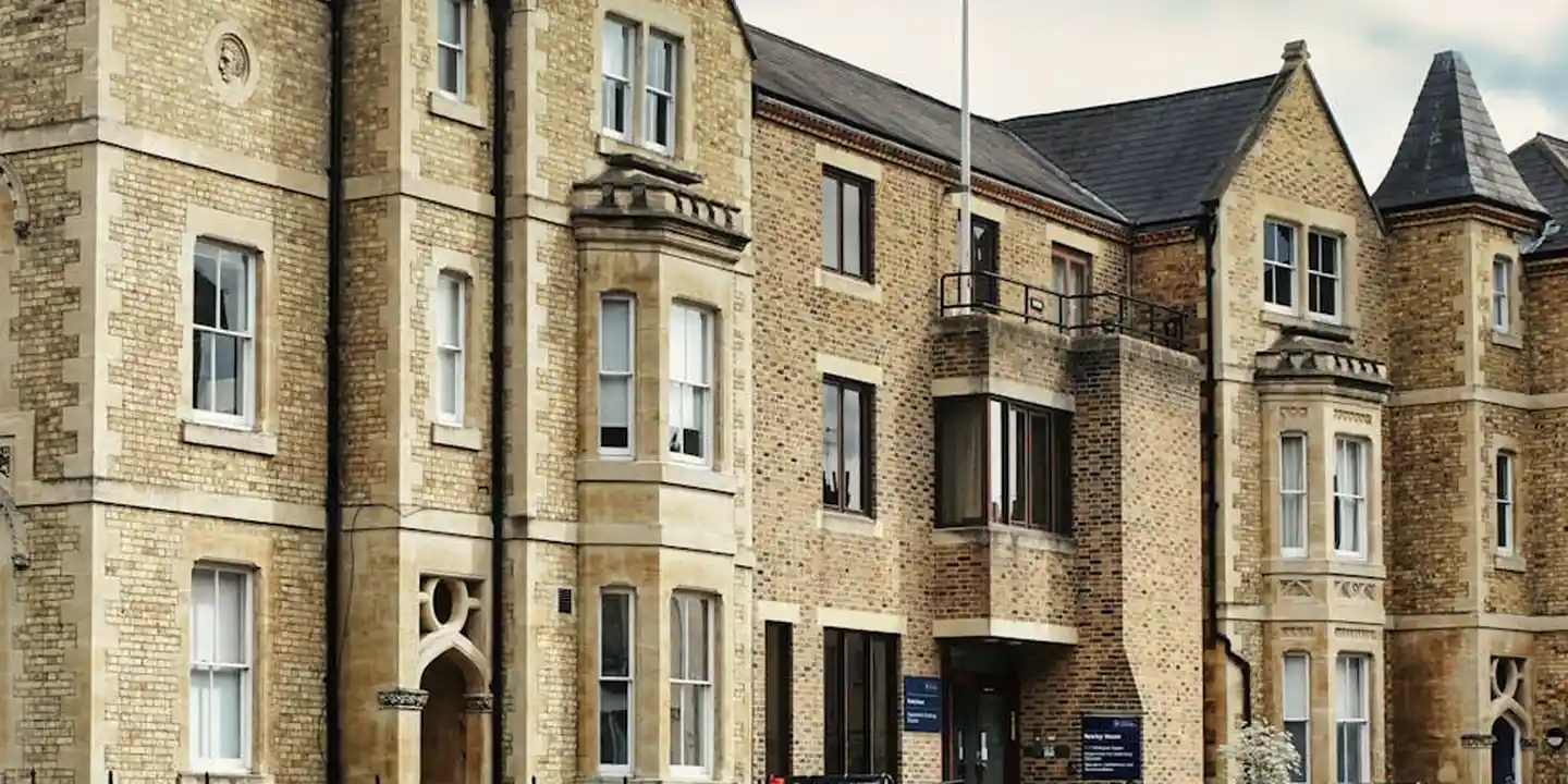 Brick residential building facade with multiple windows, balconies, and decorative masonry under a pitched roof.