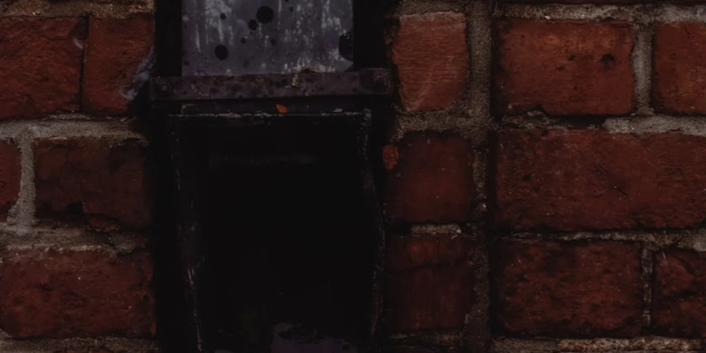 Close-up of a dark metal gutter component mounted on a red brick wall