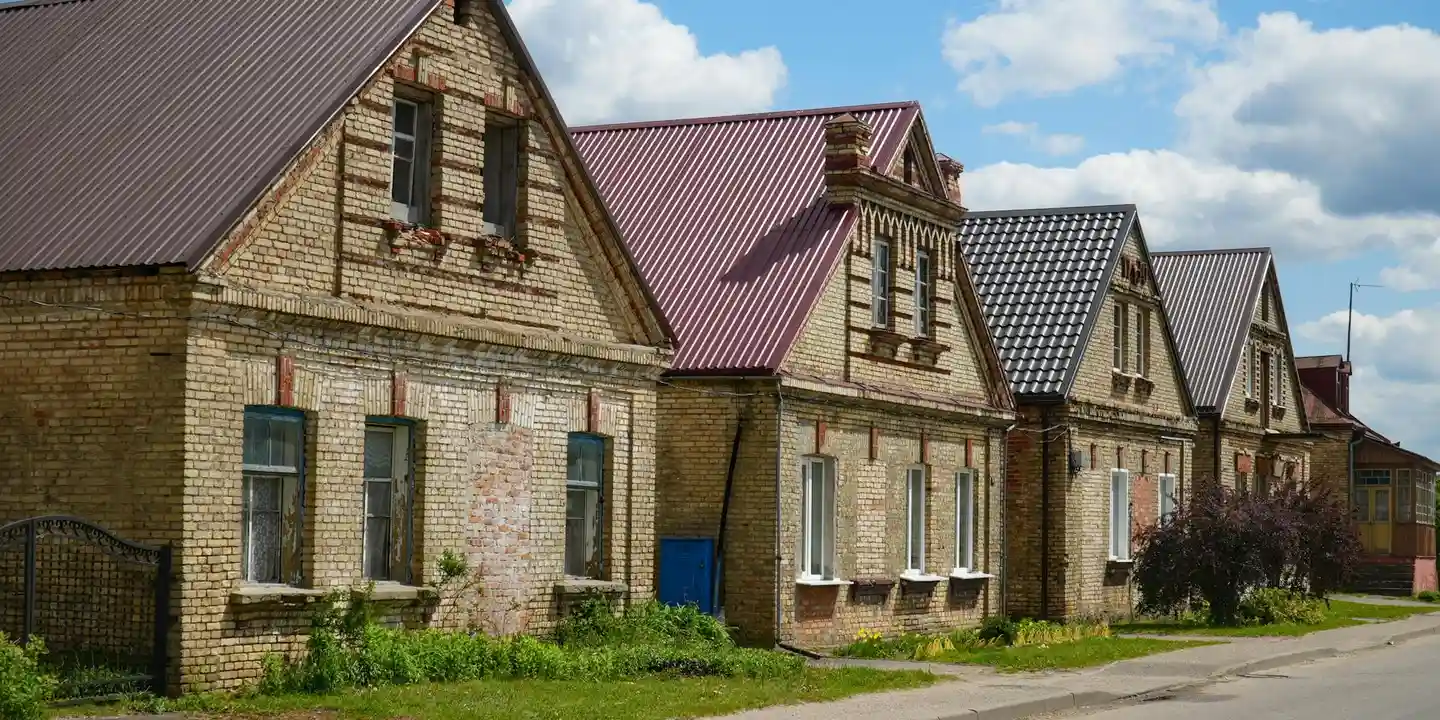 Row of brick houses with pitched gable roofs along a suburban street, featuring varying roof materials and colors.