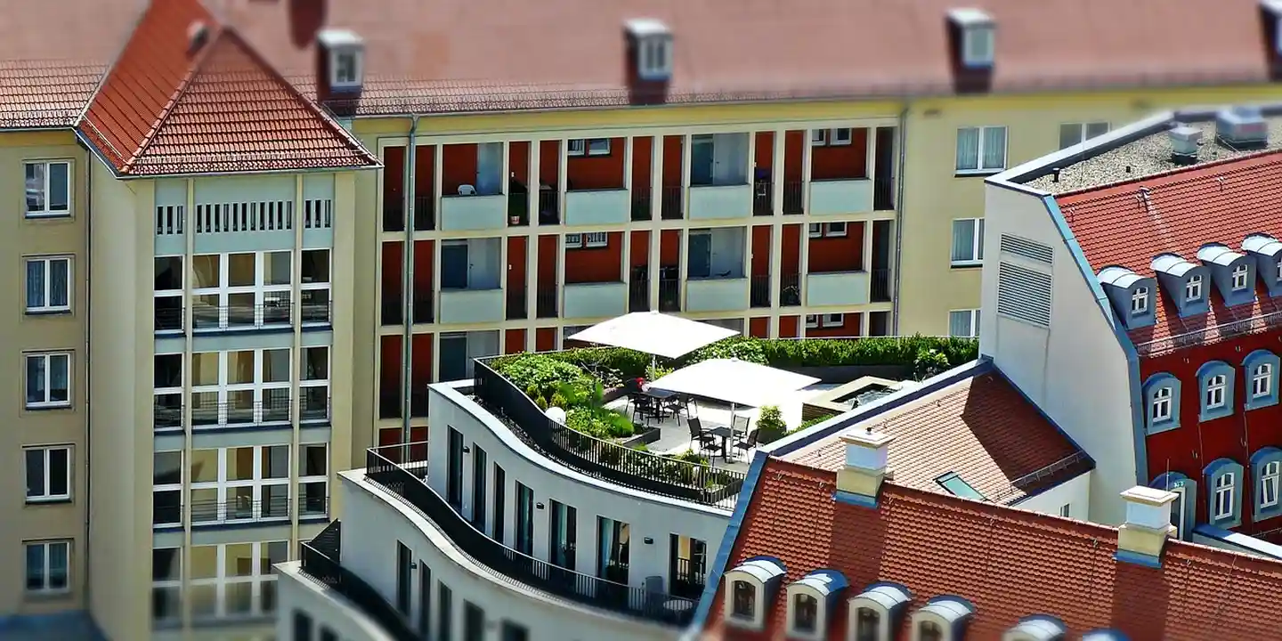 Aerial view of a block of residential buildings with red-tiled pitched roofs and a rooftop terrace, showing varied roof designs in a dense urban setting.