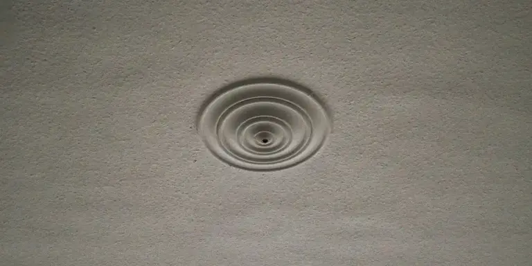 Close-up of a textured interior ceiling with a circular vent or diffuser featuring concentric rings.
