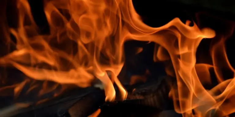 Flames rise from a charcoal chimney starter with glowing coals inside, ready for grilling.