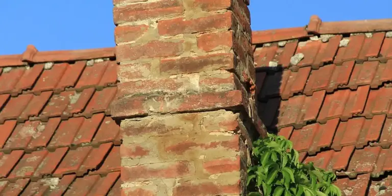 Brick chimney on a red-tiled roof with a clear blue sky