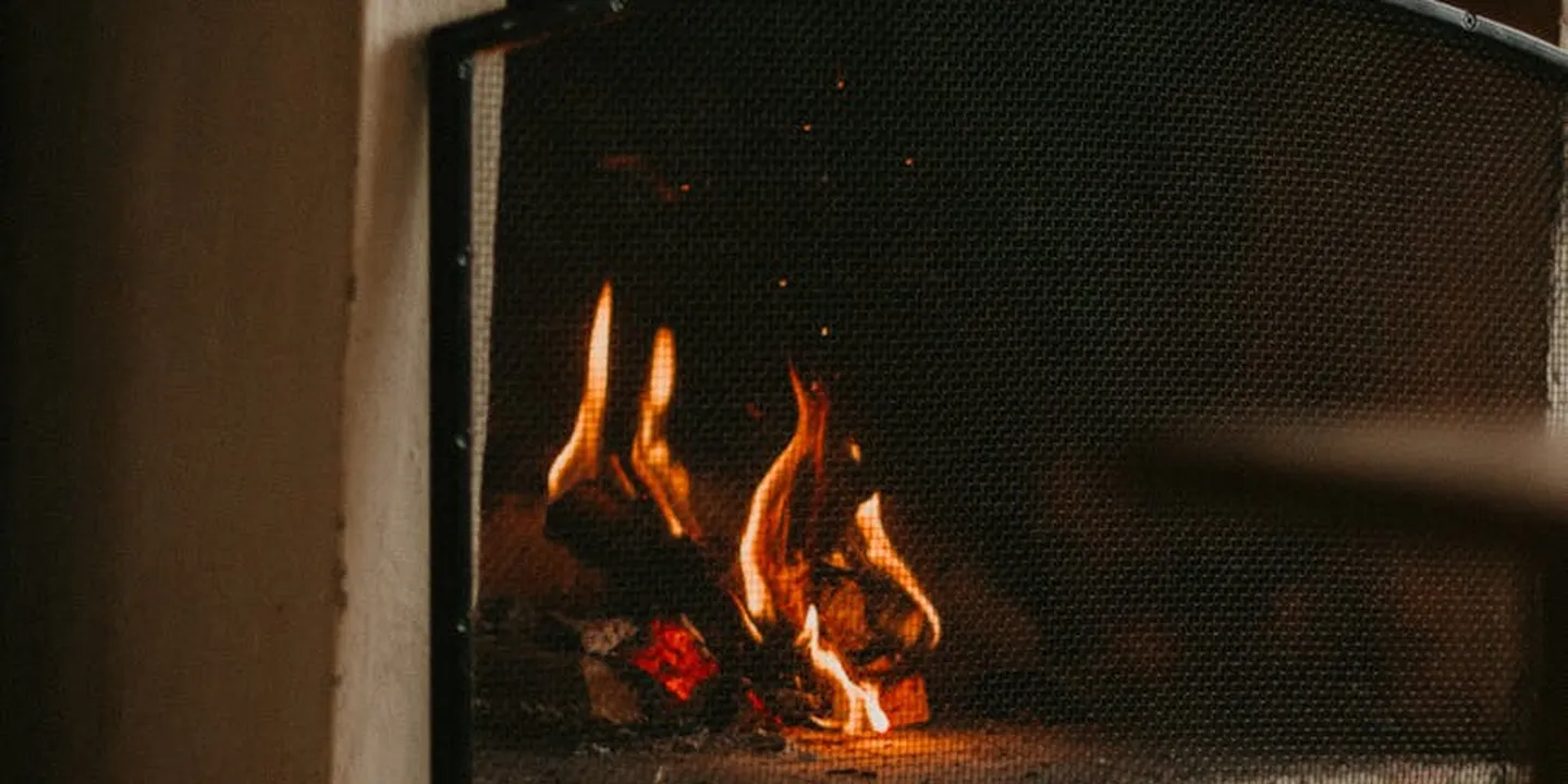 A lit wood-burning fireplace with a metal mesh screen and glowing embers