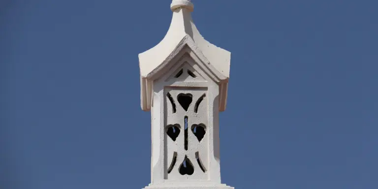 White decorative chimney vent with heart-shaped cutouts against a blue sky