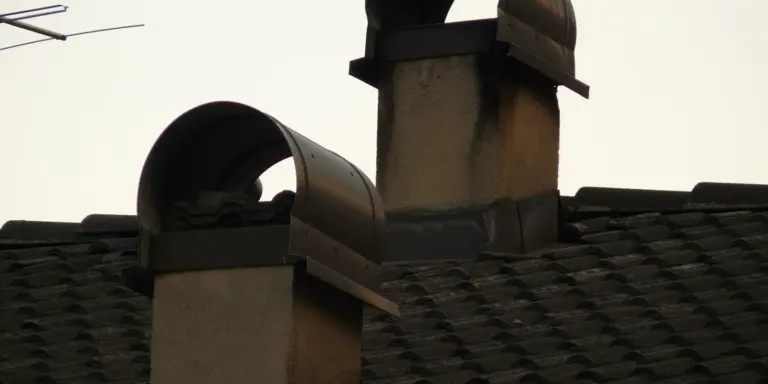 Residential roof with two chimneys; one topped with a metal cap, illustrating chimney parts and accessories.