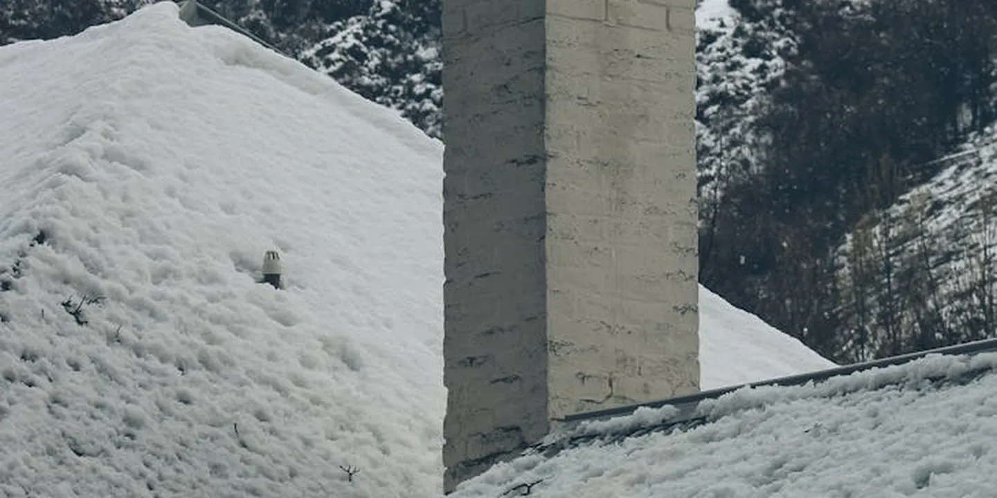 Snow-covered chimney with a protective cap atop a brick chimney on a sloped roof