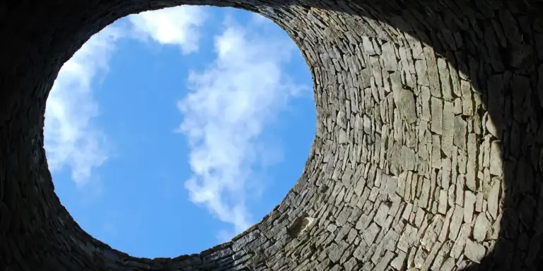 Circular brick chimney opening viewed from inside, looking up at a blue sky