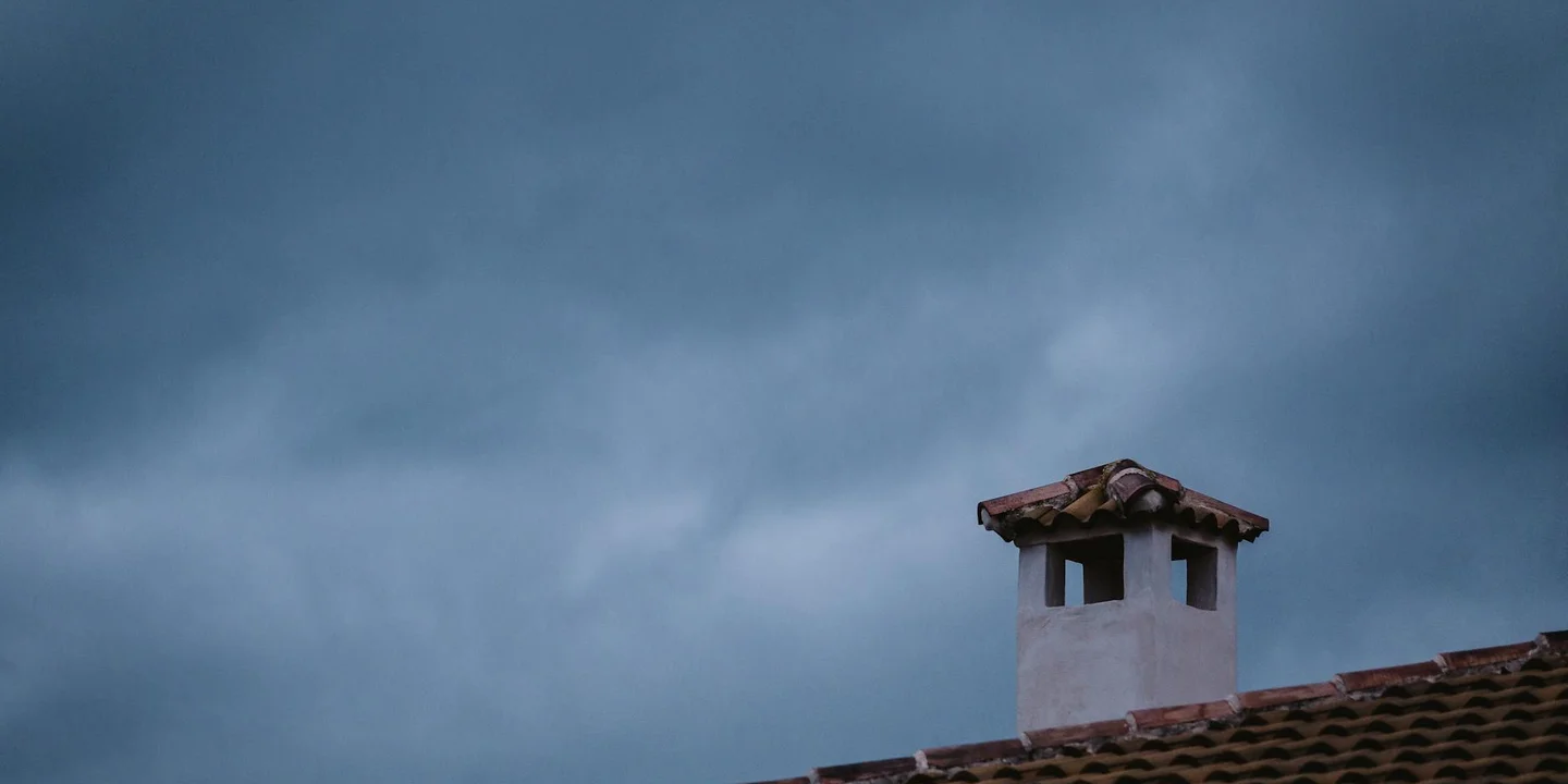 Chimney protruding from a tiled roof under a cloudy sky.