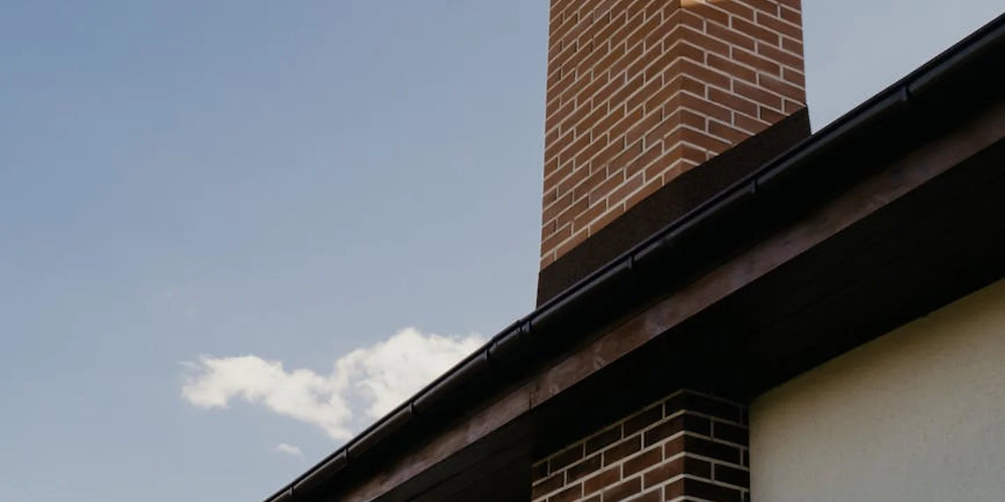 Brick chimney on a sloped roof with visible flashing and edge, illustrating where to start sealing from the top down.