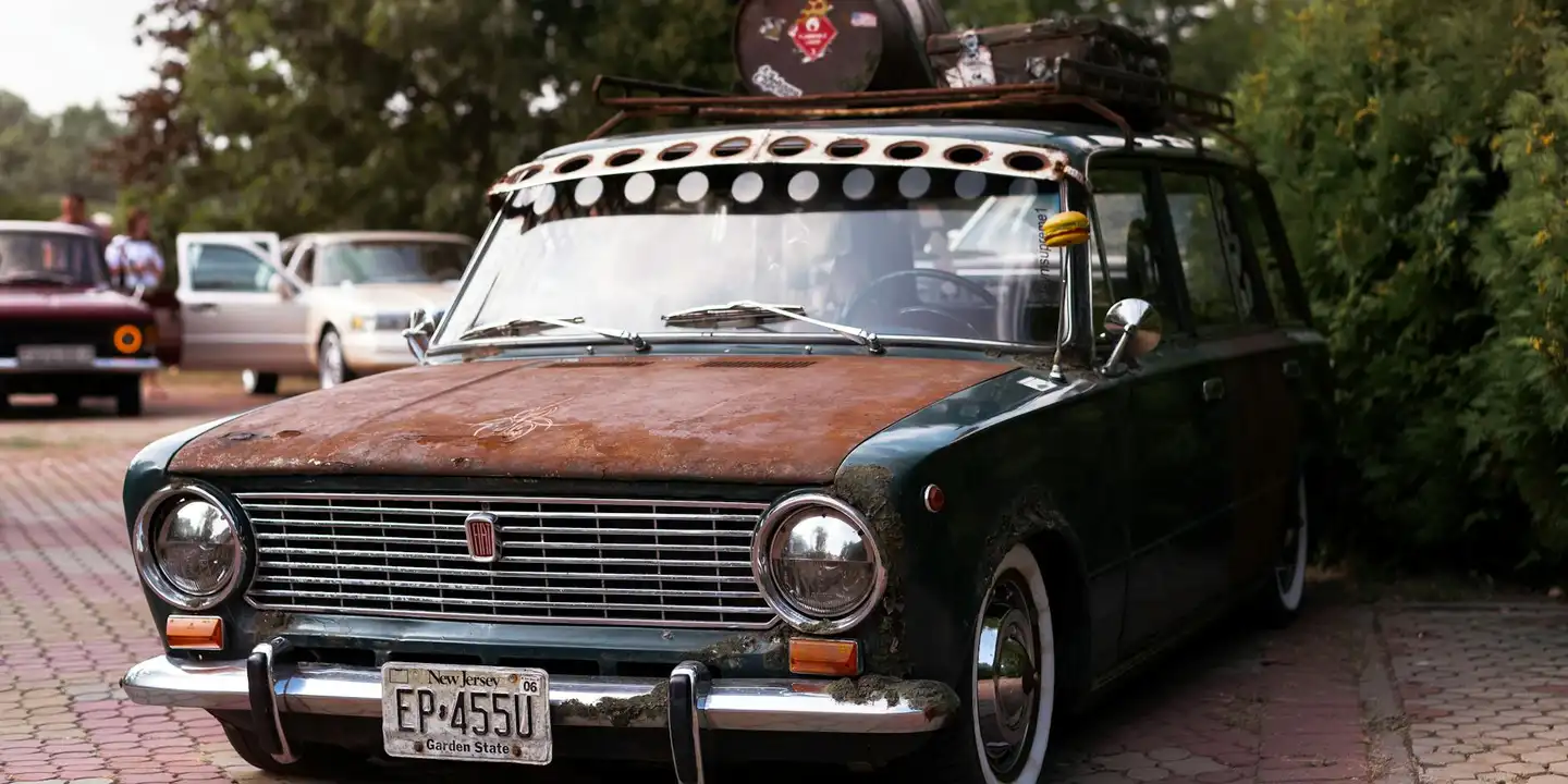 Vintage green sedan with a metal rooftop rack on top, parked on a brick driveway