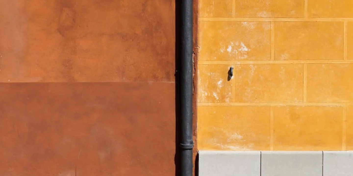 Close-up of a vertical downspout against brown and yellow brick walls, illustrating exterior gutter components.