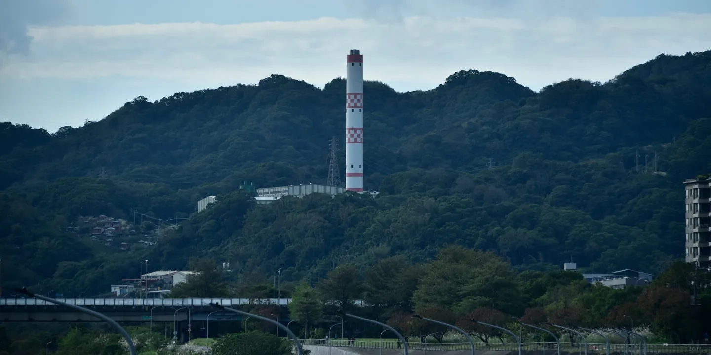 Wide shot of a forested hillside with a tall striped tower in the distance.