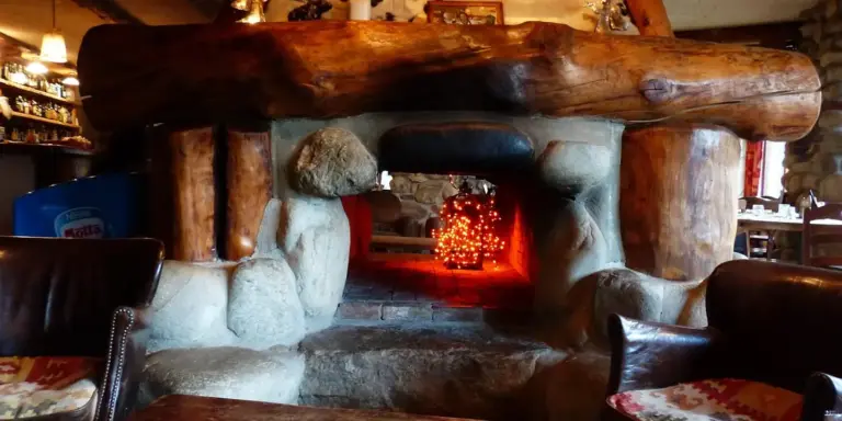 Rustic living room with a large stone fireplace, warm lighting, and a glowing hearth