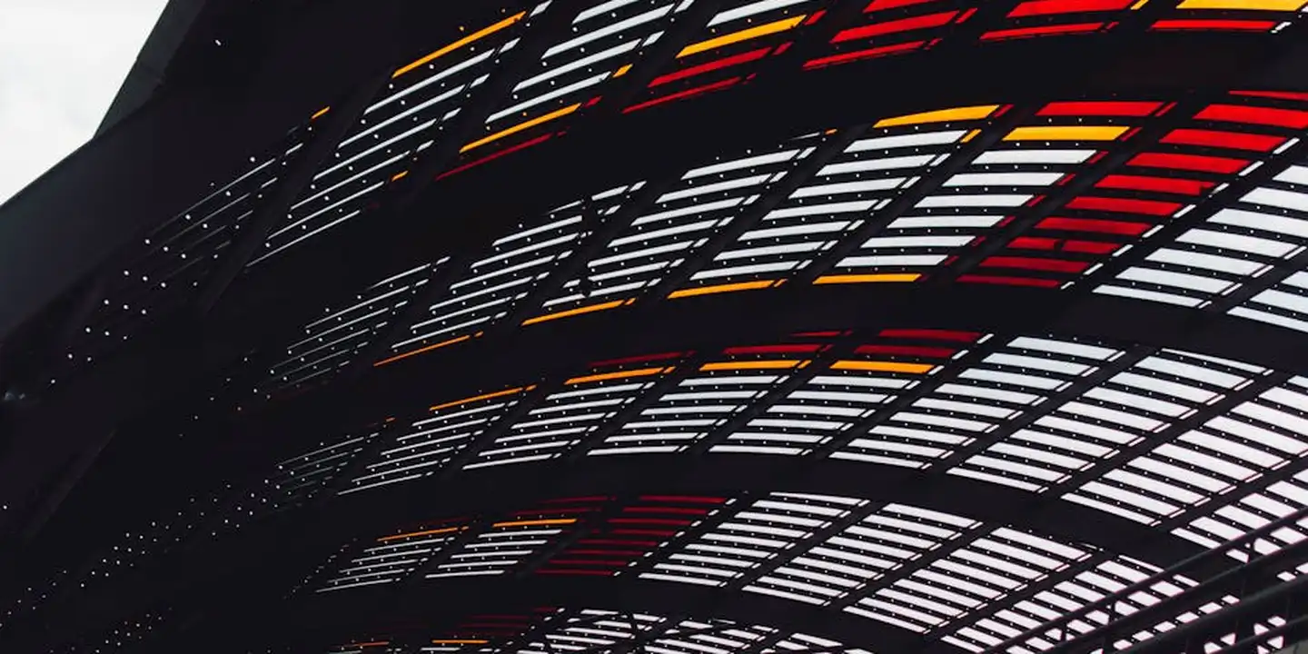 Close-up of a dark curved metal roof grid with glass panels and red accents.