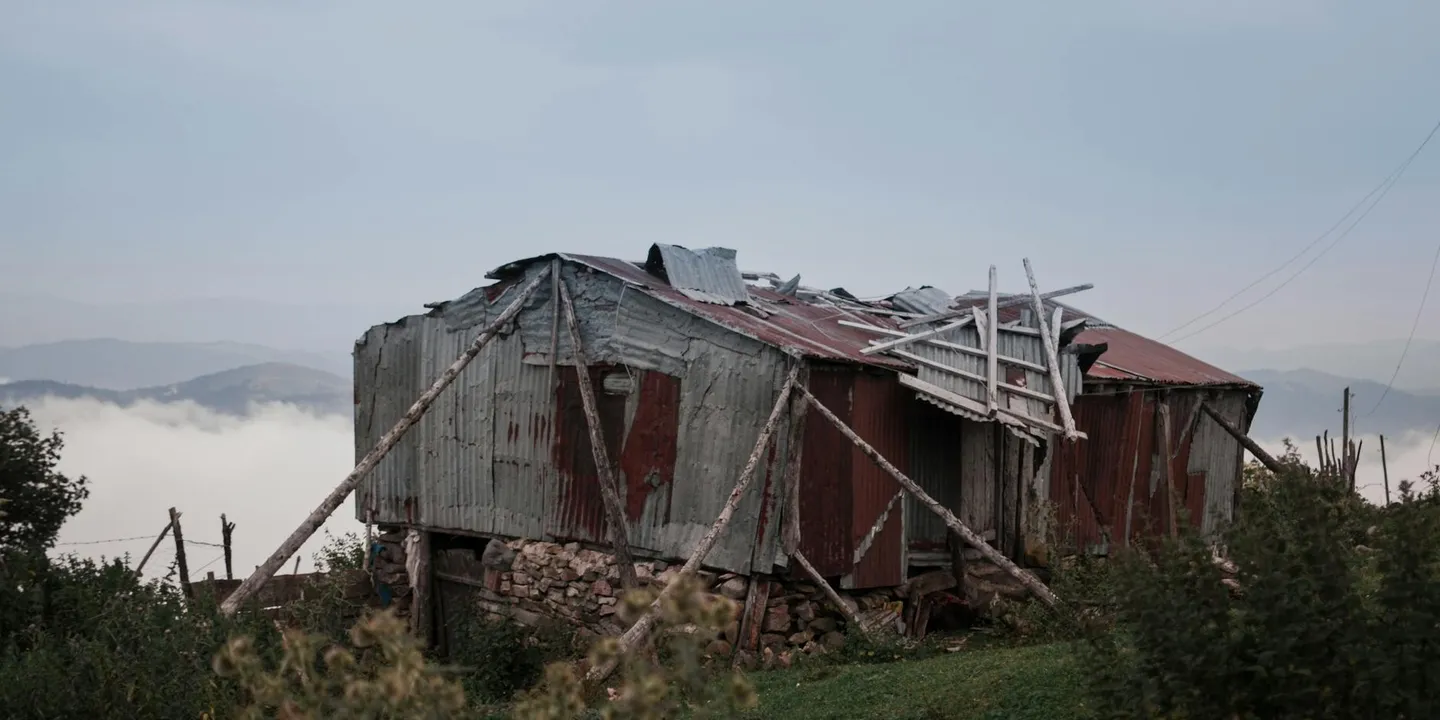 A rundown metal shed with a collapsed roof and exposed framing on a hillside.