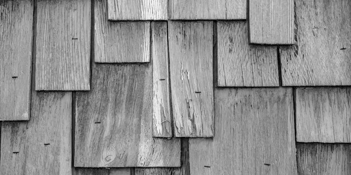 Close-up of weathered wooden shingles on a dormer roof, showing overlapping shingles and rough textures.