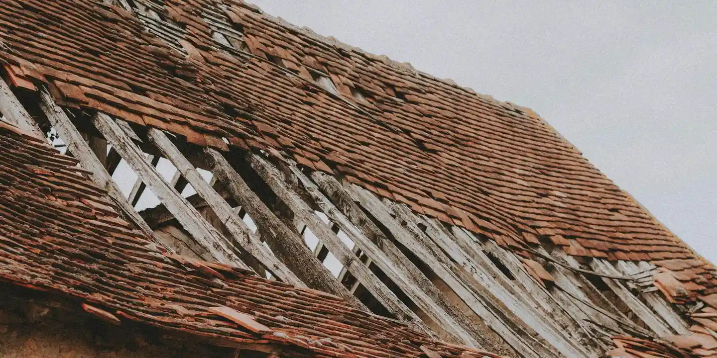 Close-up of a dormer-style roof with missing shingles exposing the underlayment and wooden structure at the valleys and flashing.