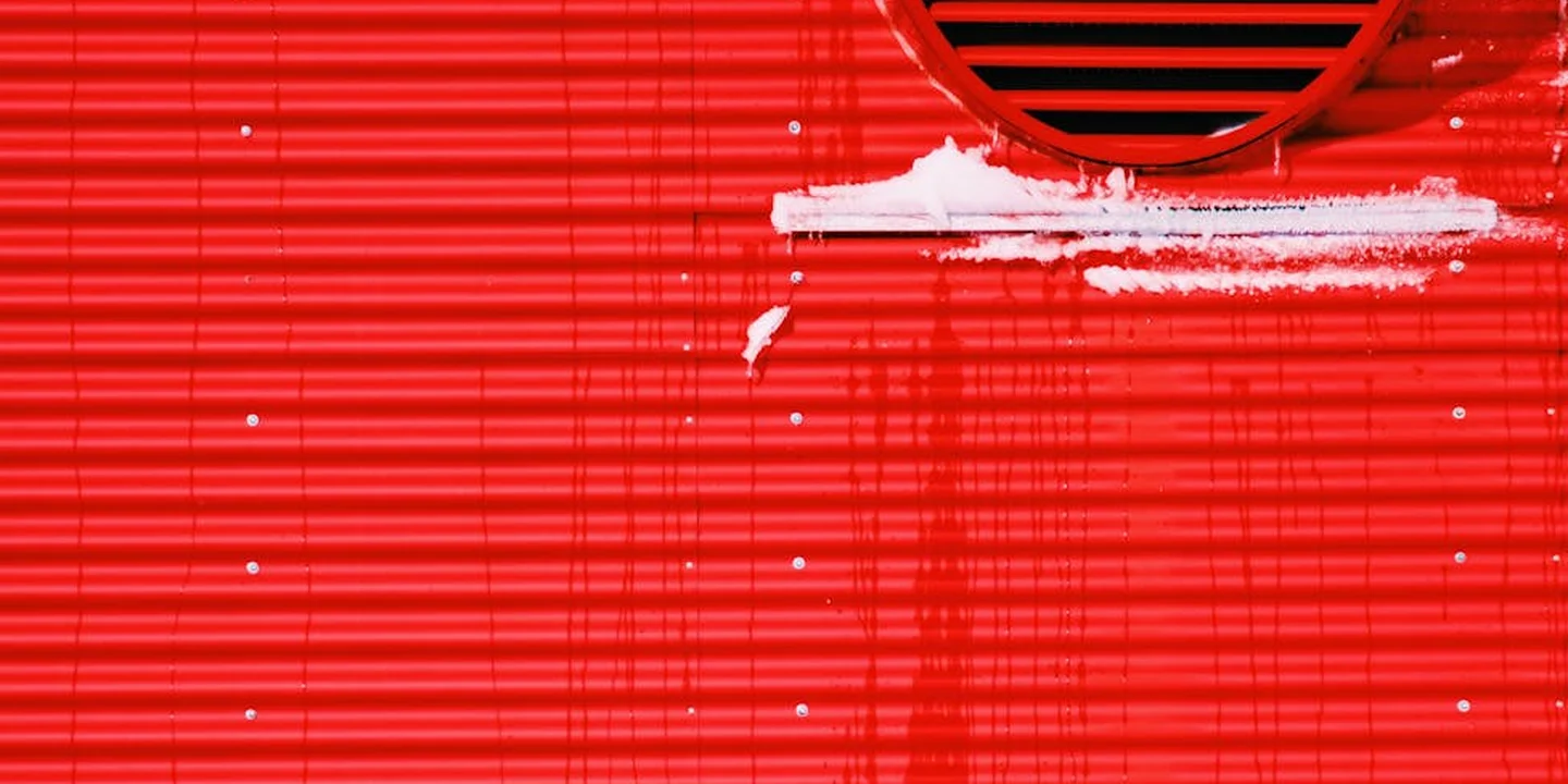 Circular roof vent on a red exterior surface with white sealant along the edge