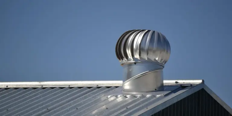 Metal dryer vent pipe protruding through a metal roof with a vent cap
