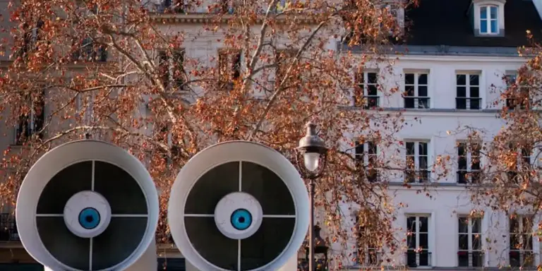 Two large circular vent hoods mounted on an exterior wall with autumn trees and white buildings in the background.