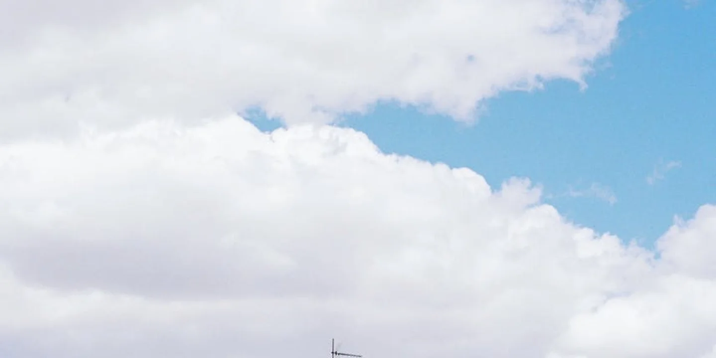 Blue sky with scattered clouds above a flat roof edge and a roof vent, illustrating a roof inspection.