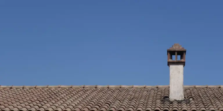 Clay tile roof with a chimney and a clear blue sky