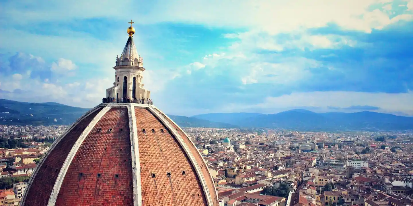 Dome of Florence Cathedral (Duomo) rising above a cityscape with red-tiled roofs under a blue sky.