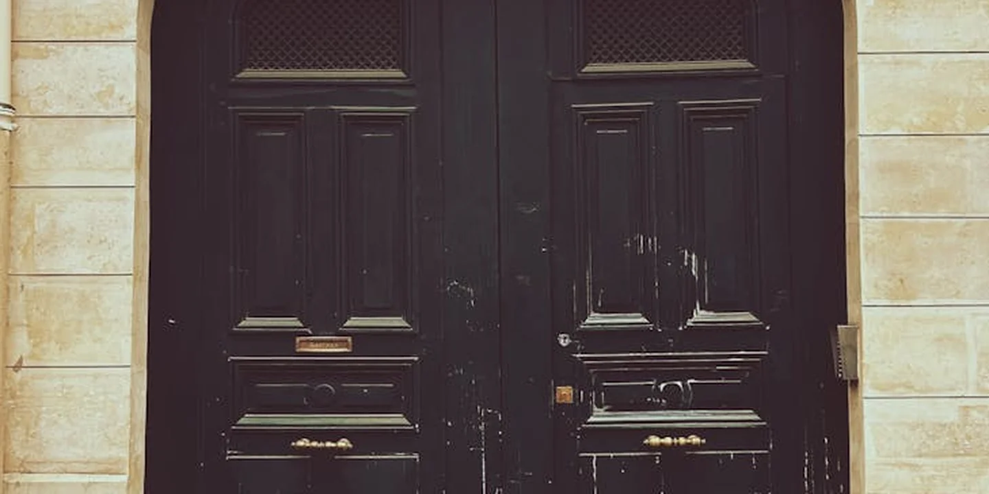 A pair of dark, paneled double doors set into a light stone facade