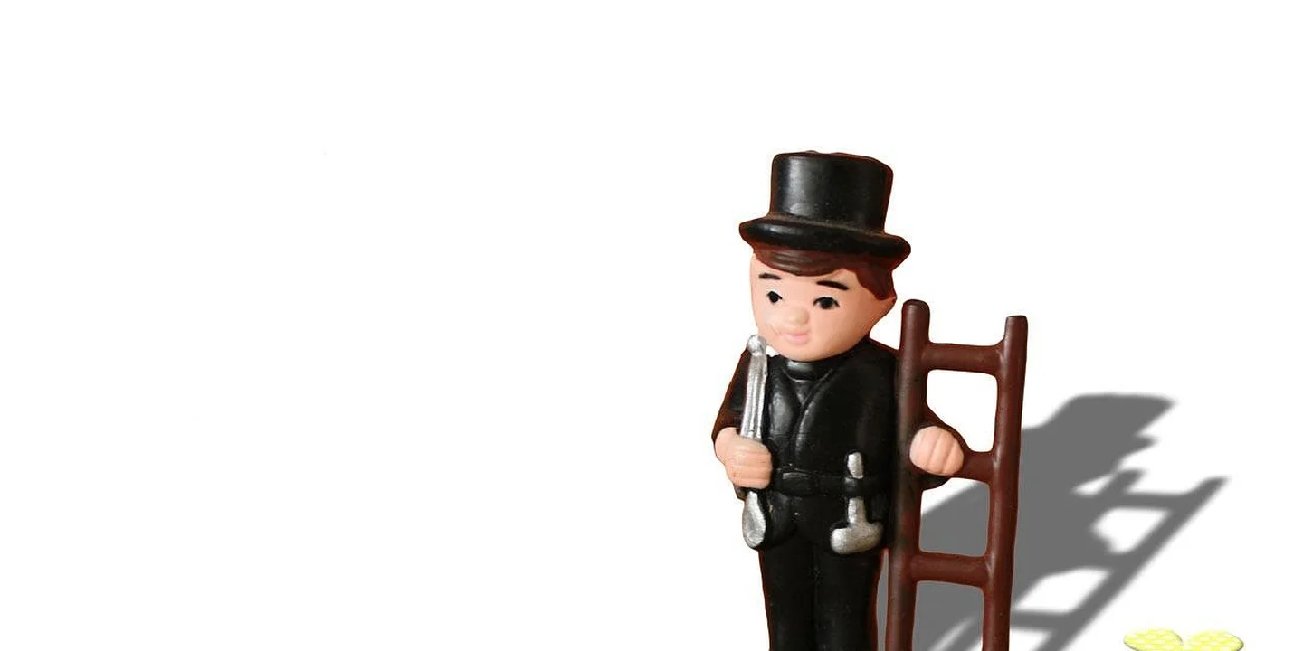 Small chimney sweep figurine with a top hat and brush, standing against a white background with a shadow