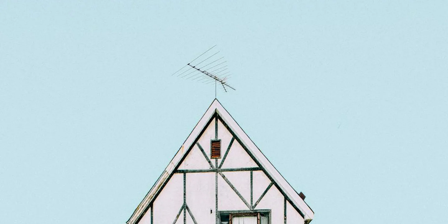 Gable roof with white trim and antenna against a pale blue sky.