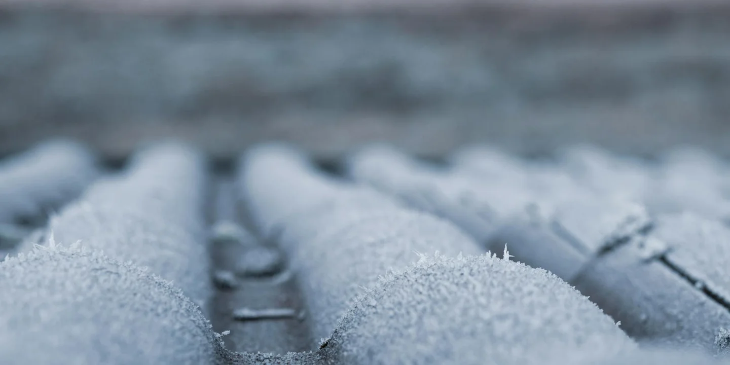 Close-up of frost-dusted roof shingles on a sloped surface, illustrating the texture of a gambrel-style roof.
