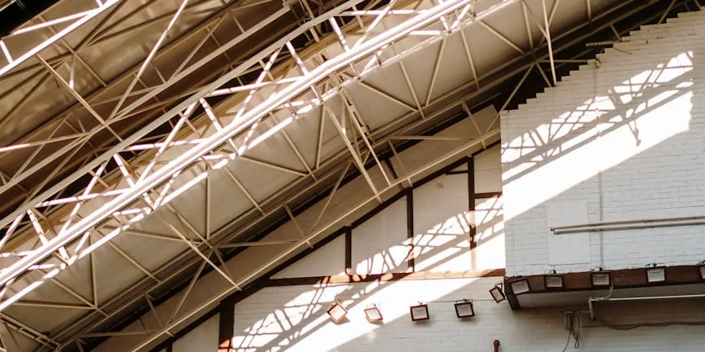 Interior of a workshop showing metal roof trusses and steel framing with sunlight casting shadows.
