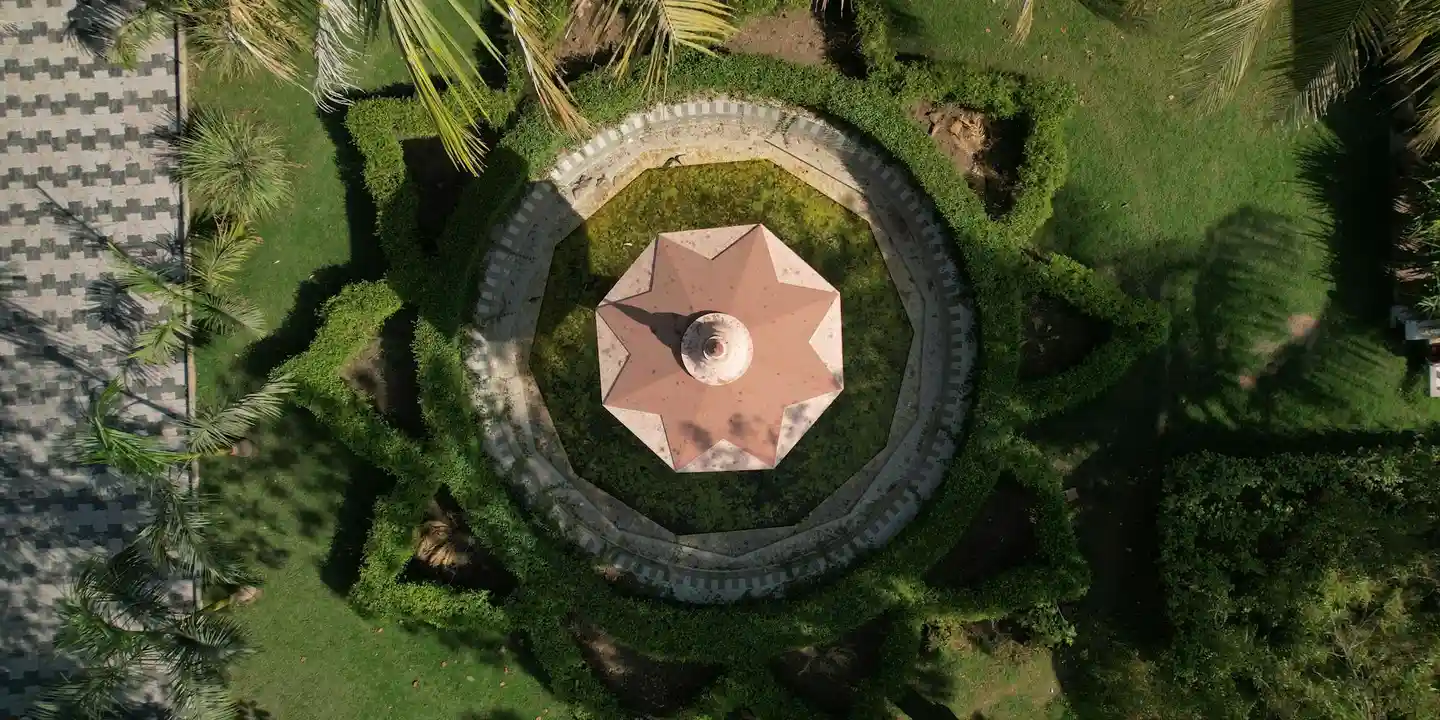 Aerial top-down view of a circular stone gazebo with a pink canopy, surrounded by a circular path and lush green lawn.