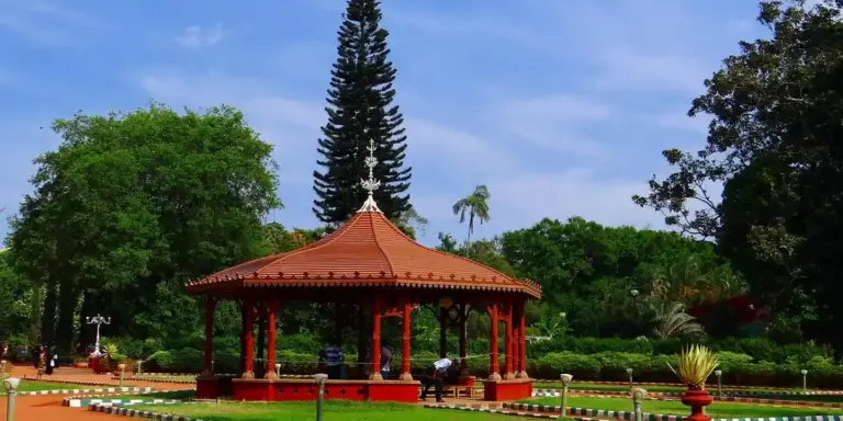 Red-roofed gazebo in a park with lush green trees and a blue sky