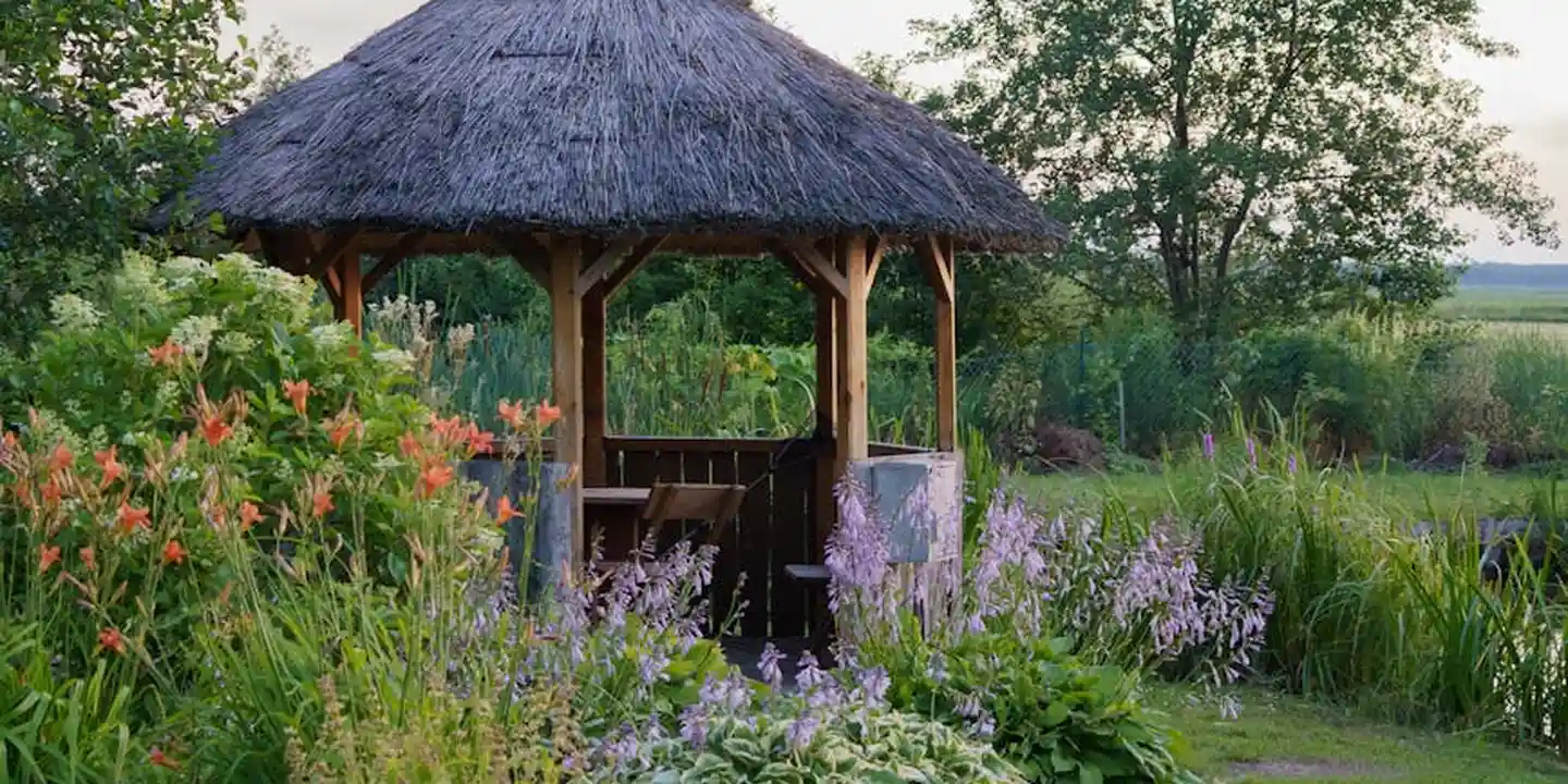 A gazebo with a thatched roof in a lush garden.