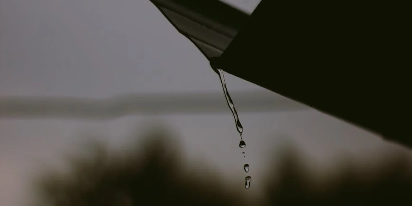 Water dripping from a gutter edge with a blurred background, illustrating gutter maintenance.
