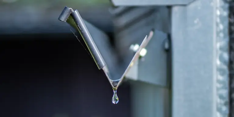 Close-up of a metal gutter elbow with a water droplet, illustrating water management during roof replacement