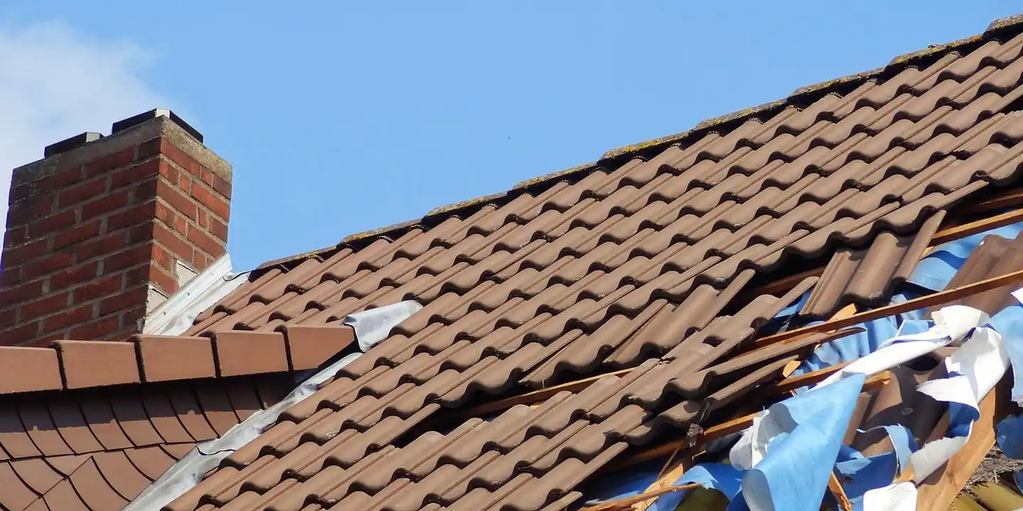 Clay tile roof with visible hail damage, including cracked and displaced tiles and scattered debris against a clear blue sky.
