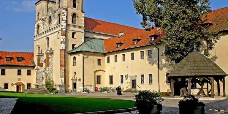 Historic building with a red-tiled roof, stone walls, and a wooden gazebo in a manicured courtyard.