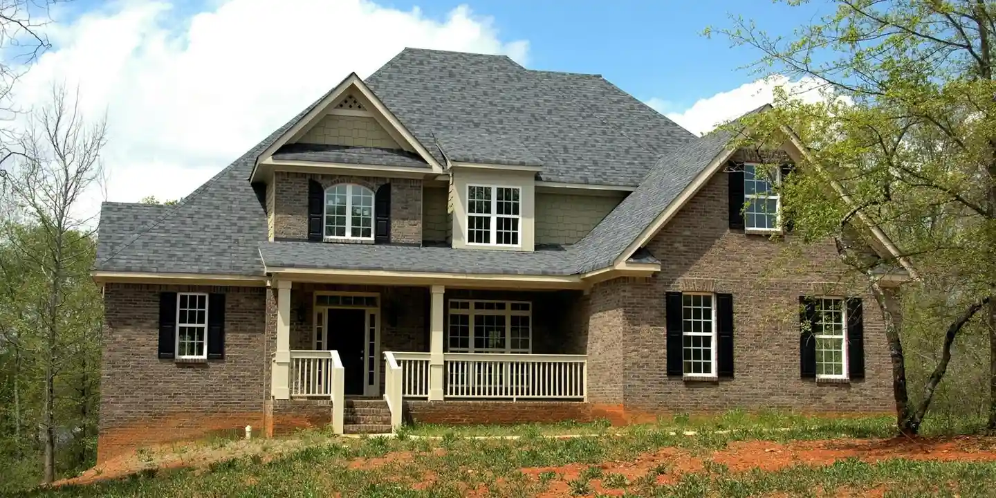 Brick suburban house with a large dark shingle roof and a small front porch, surrounded by trees.