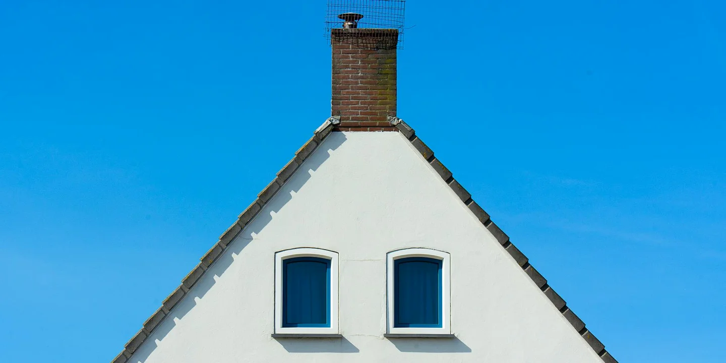 White house with a steep triangular roof and a brick chimney against a bright blue sky