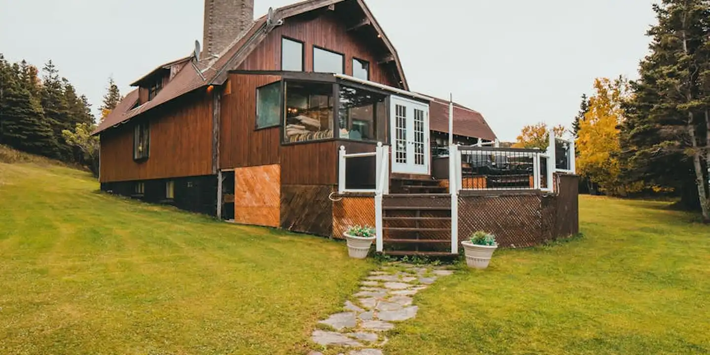 Residential house with a brick chimney on the roof, wooden siding, and a stone path across a green lawn.